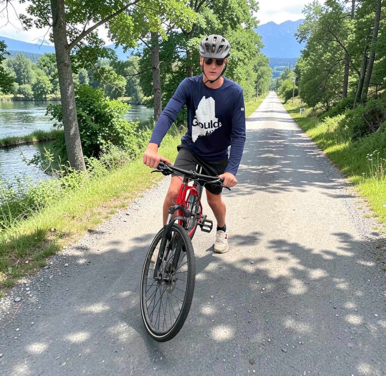 Nick Cornell in a helmet and Gould Academy shirt, standing over his bike on a waterside trail